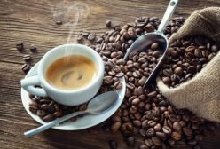 Cup of espresso with coffee beans, bag, scoop and steam on rustic wooden background